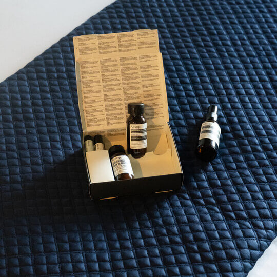 A box of travel-sized Aesop formulations on a navy quilt.