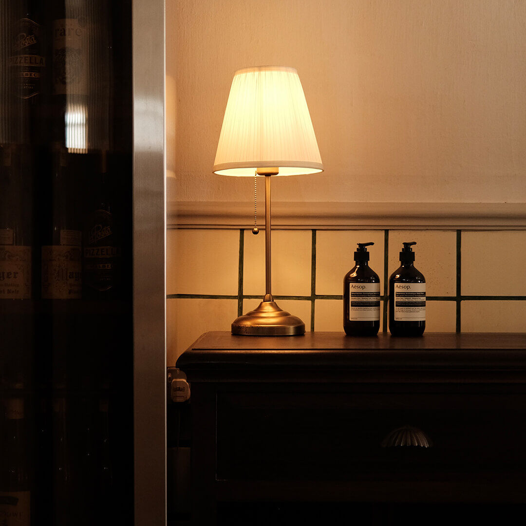 Two Aesop bottles on an entry table alongside an antique lamp.
