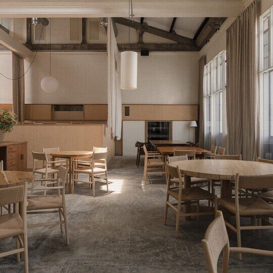 An empty restaurant with high ceilings, timber tables and chairs, and hanging pendant lights.