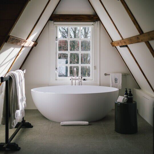 A freestanding bathtub in front of a window, alongside Aesop formulations—all under an A-frame ceiling.