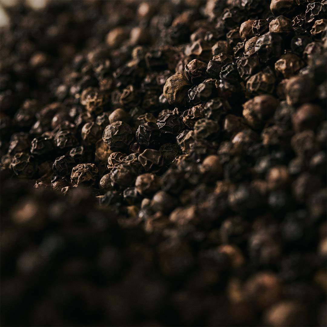 Close-up of black peppercorns scattered across a dark textured surface.