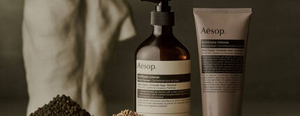 Aesop Antithesis Intense Body Cleanser pump bottle and tube beside piles of black peppercorns and coriander seeds.