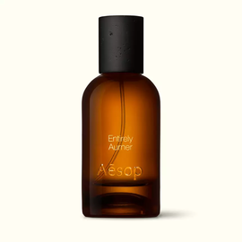 Amber glass Aesop Entirely Aurner Eau de Parfum bottle with black cap on a white background.